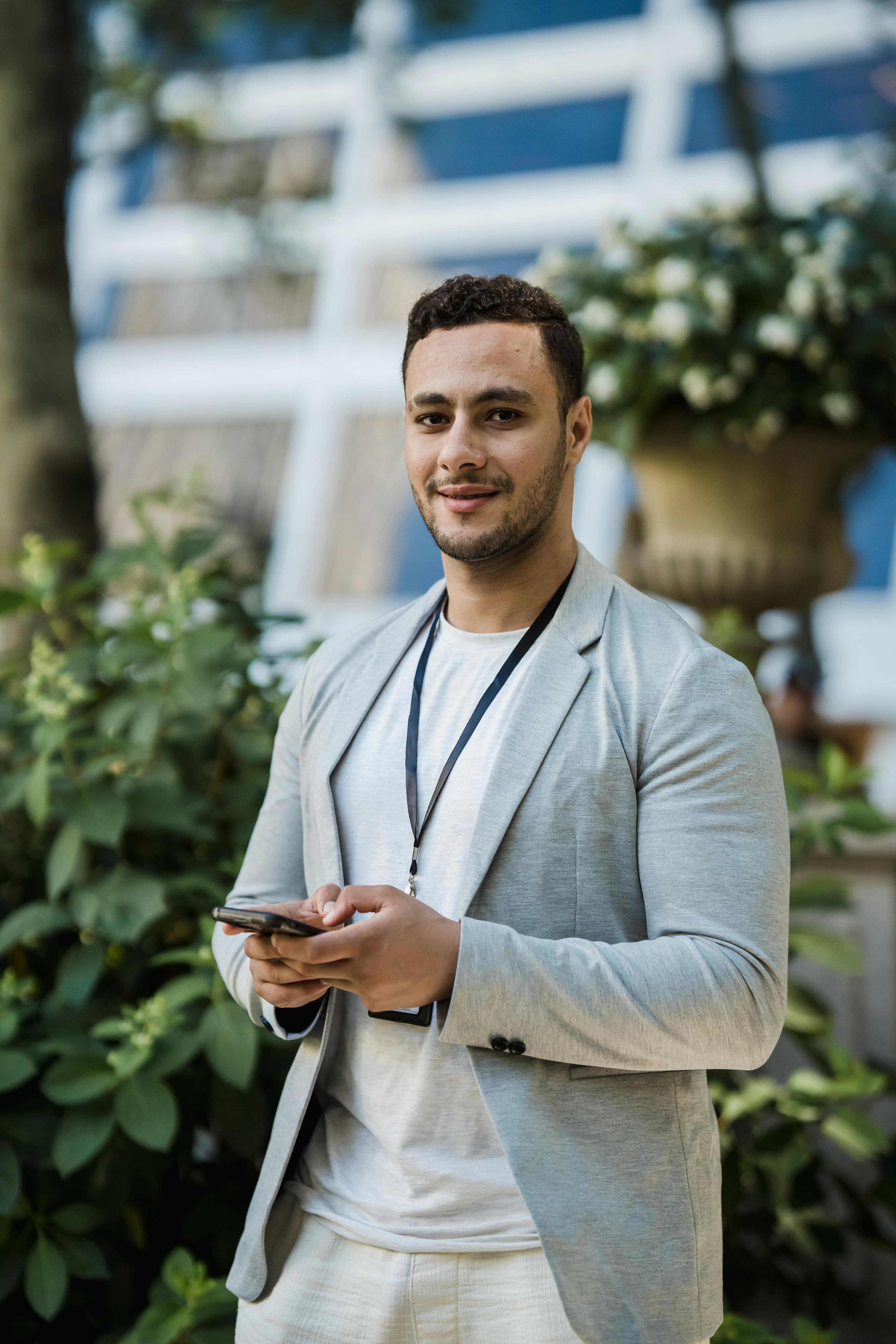 A young professional wearing a lanyard ID badge and holding a phone outdoors