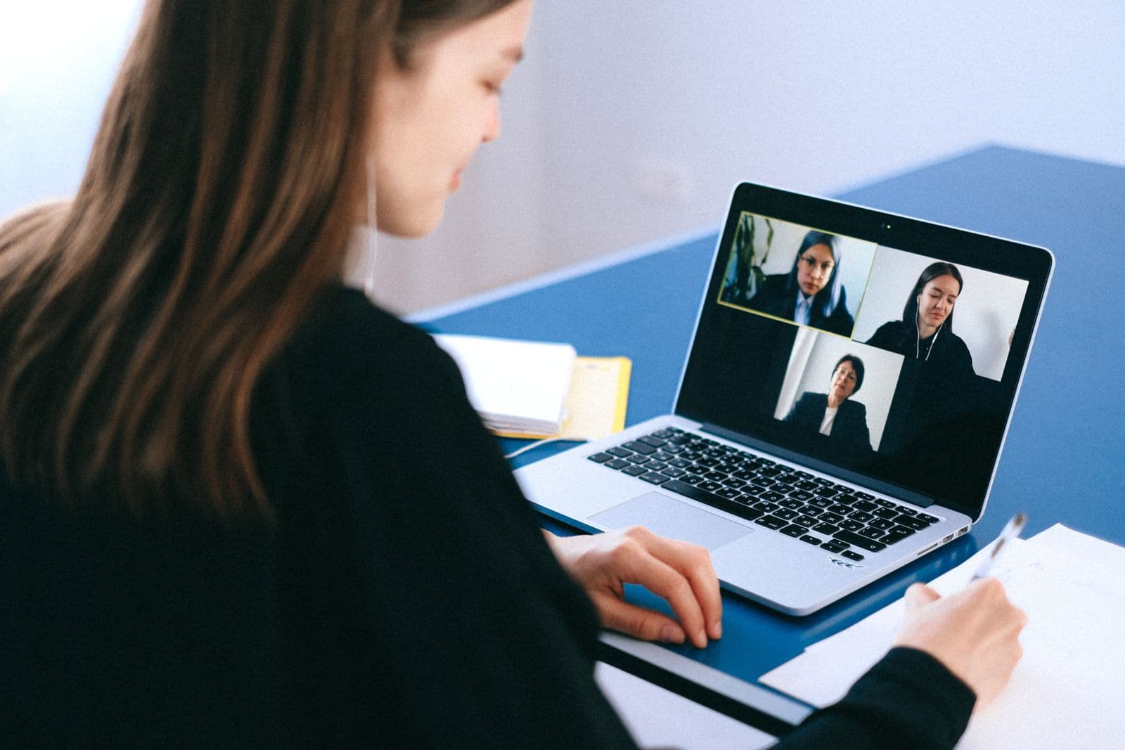 A person on a laptop video call with three remote participants shown on screen